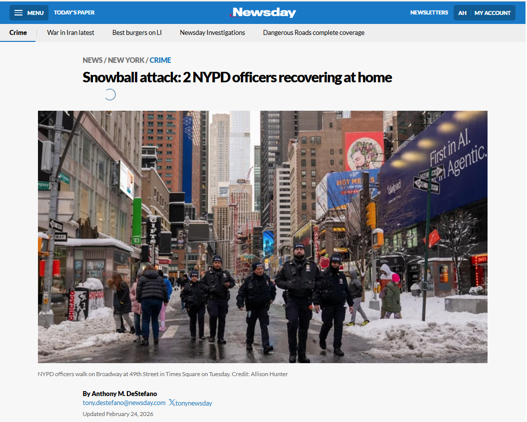 Four NYPD officers walk abreast on Broadway near 49th Street in Times Square, with snow piled along the sidewalks and the city's skyline and billboards visible behind them.