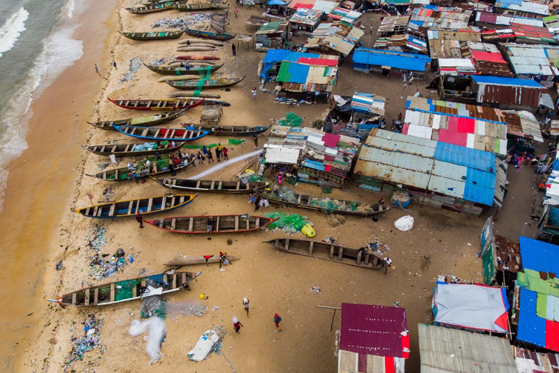 An aerial photograph of West Point, an informal fishing settlement, with wooden canoes and tin-roofed structures steps from the shore.